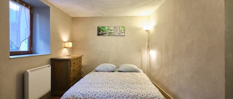 A bedroom with a bed, a dresser, a radiator, a window with curtains, and a wall-mounted picture.