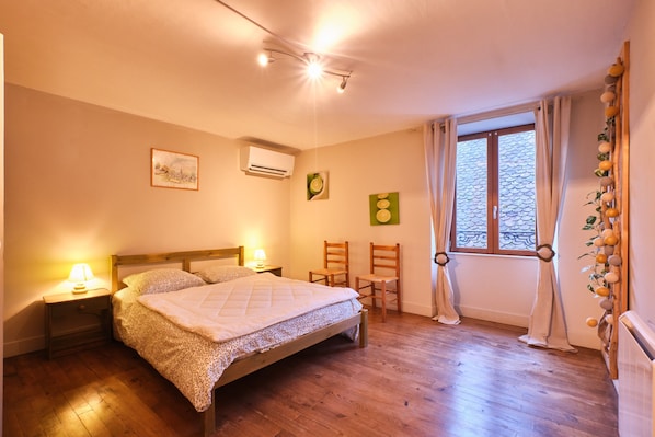 A bedroom with a bed, bedside lamps, a window with curtains, and a wall-mounted air conditioner.