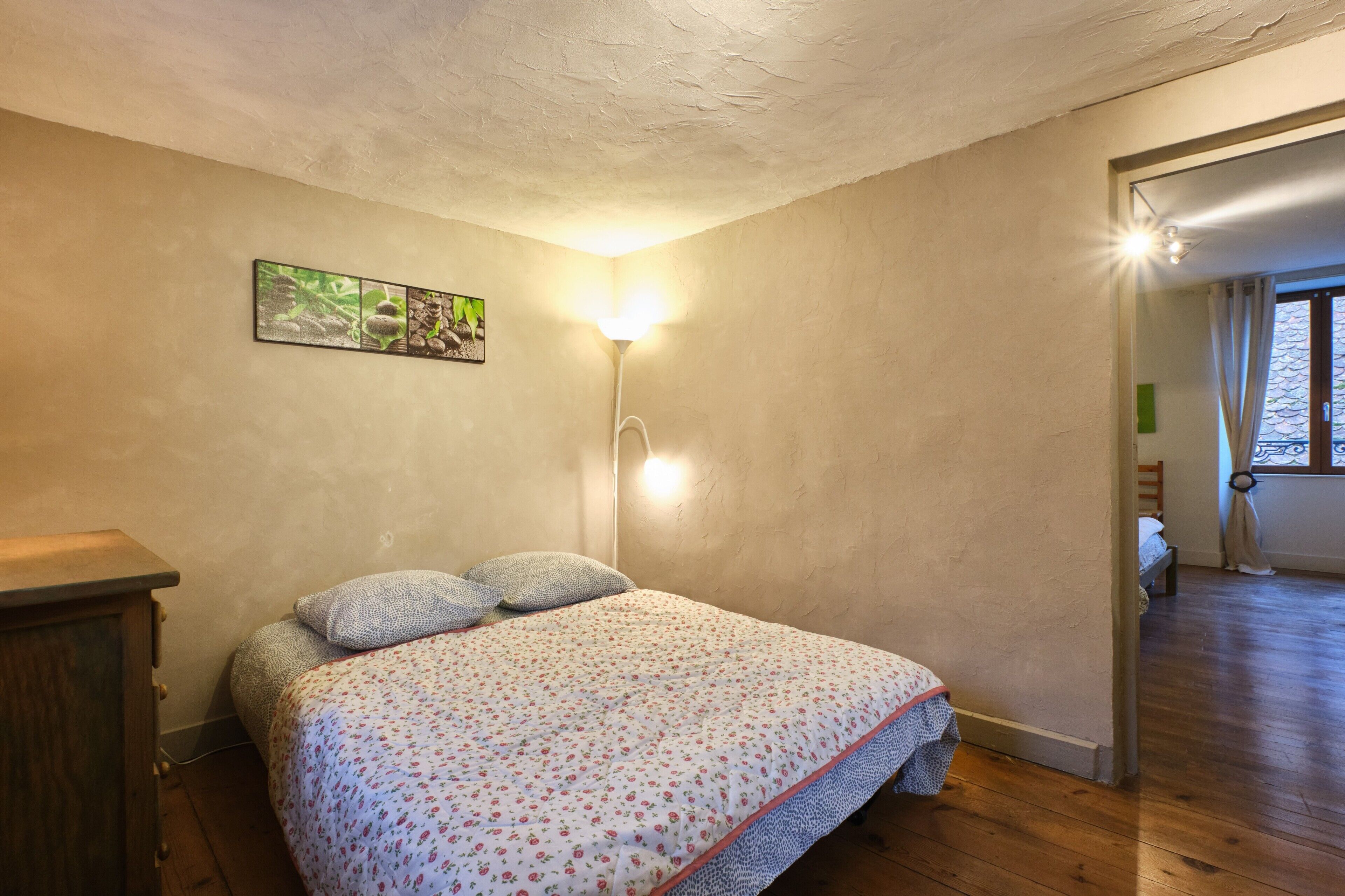 A bedroom with a bed, a nightstand, a wall-mounted lamp, and a painting.