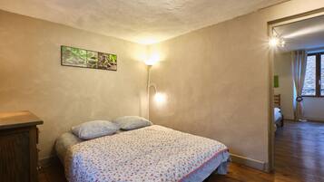A bedroom with a bed, a nightstand, a wall-mounted lamp, and a painting.