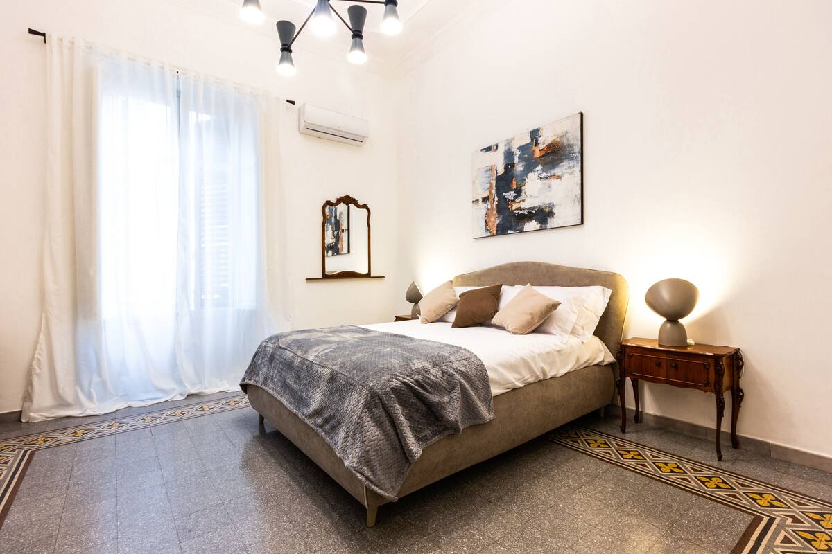A bedroom with a bed, a bedside table, a lamp, a mirror, and a painting on the wall.