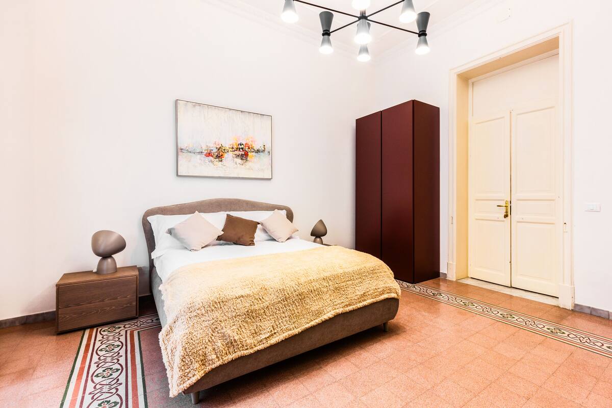 A bedroom with a bed, a nightstand, a wardrobe, a door, and a ceiling light fixture.