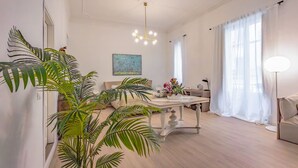 A modern living room with a wooden floor, a dining table, a sofa, and large green plants. - Kepos Rooms & Suites (Palermo)