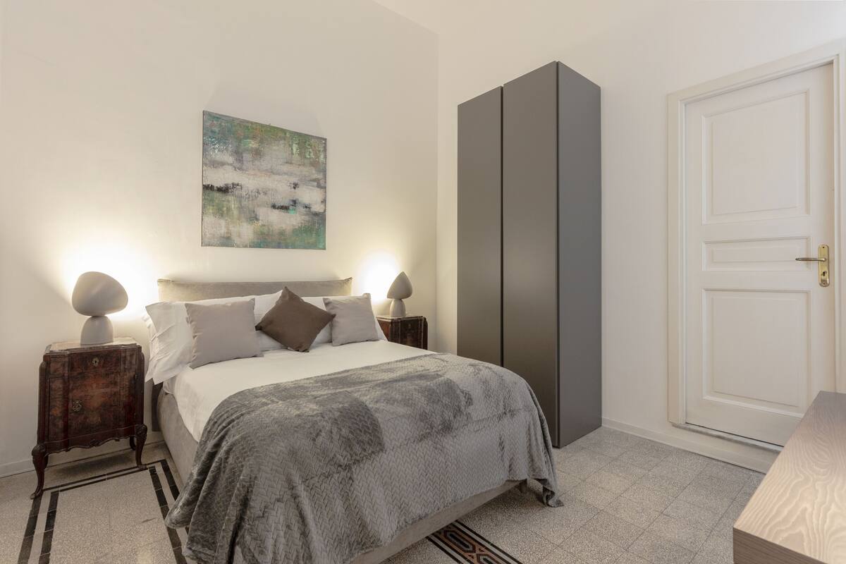 A bedroom with a bed, bedside tables, a painting, a wardrobe, and a door.