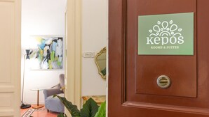 A hotel room with a green sign reading "kepos rooms & suites," a mirror, a "Welcome" sign, a modern chair, and a large abstract painting. - Kepos Rooms & Suites (Palermo)