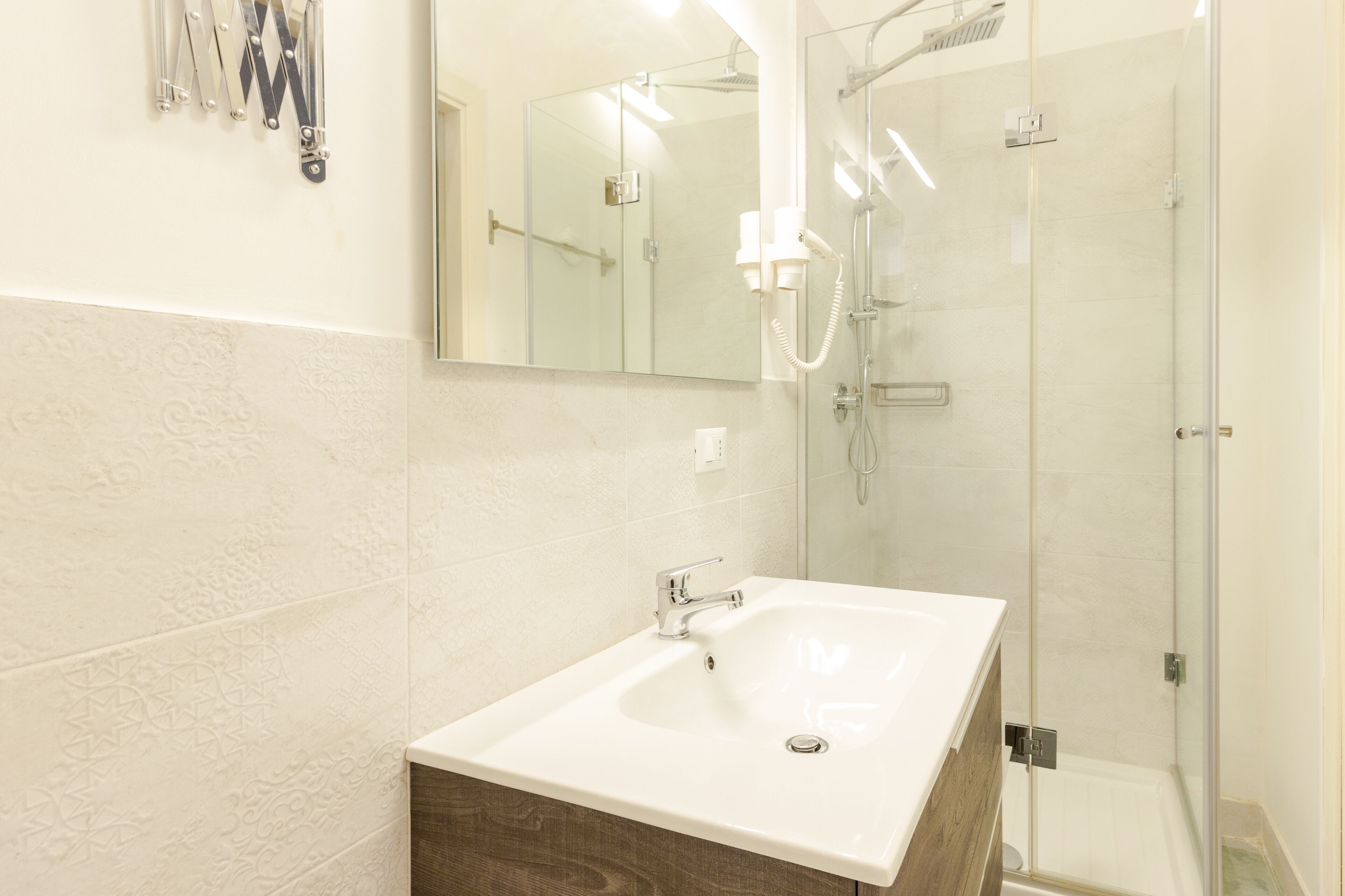 A bathroom with a large mirror, a sink, and a glass-enclosed shower.