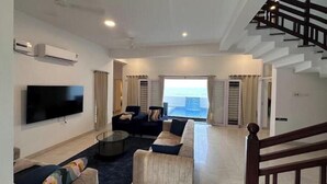 Een moderne woonkamer met een flatscreen televisie, banken, een bijzettafeltje en een groot raam met uitzicht op zee.