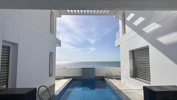 Een overloopzwembad met uitzicht op de oceaan, omringd door witte muren en een pergola.