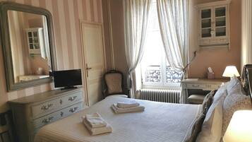 Une chambre d’hôtel comprenant un lit, une commode, un miroir, une télévision, une fenêtre avec des rideaux et un radiateur.