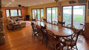 A spacious dining area with a large wooden table and chairs, a ceiling fan, and a view of a deck through glass doors.
