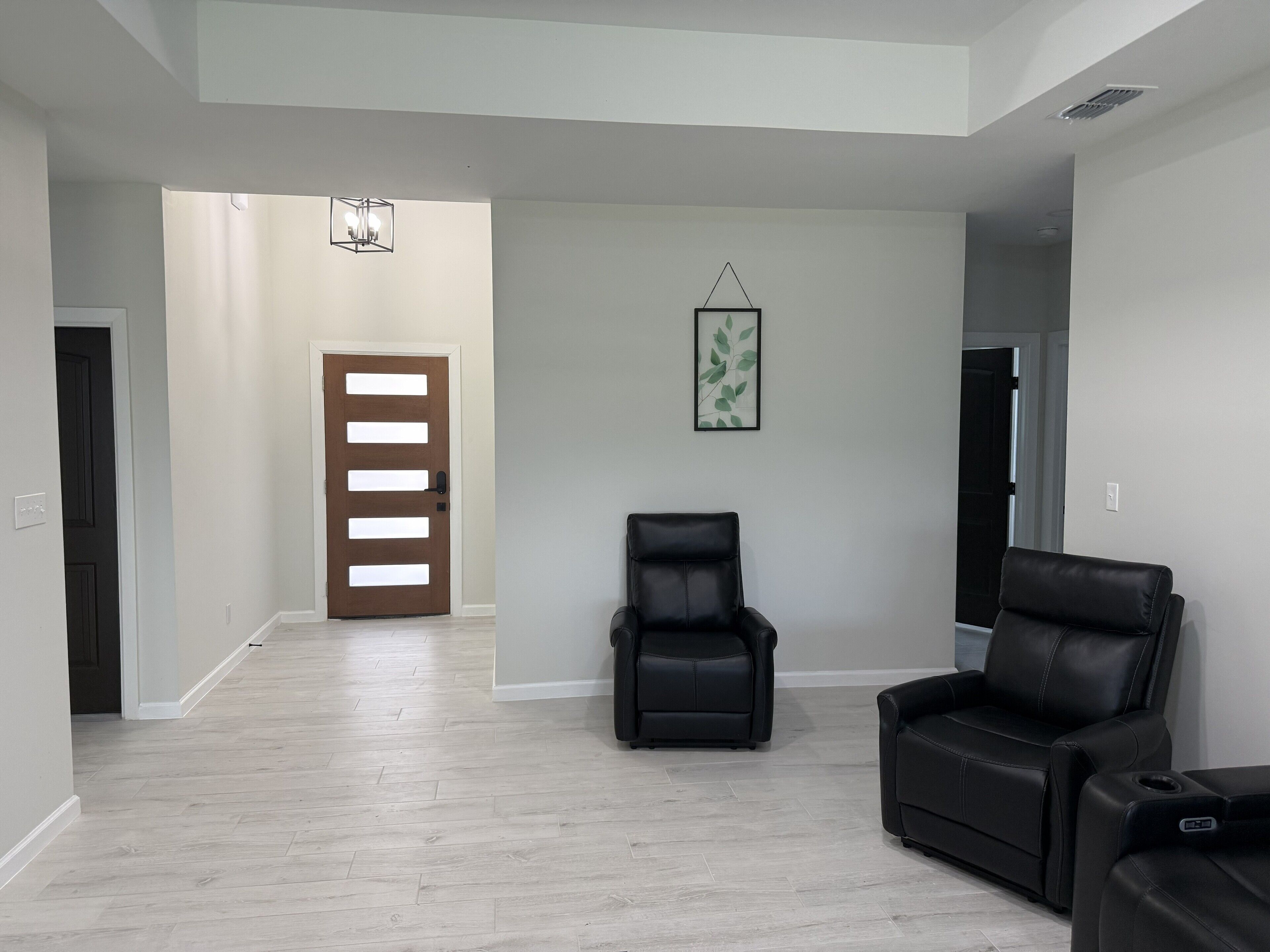 Un vaste espace de vie agrémenté d’une porte en bois, d’un fauteuil en cuir noir et d’un canapé en cuir noir.