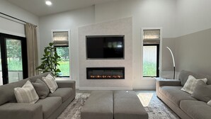 Een moderne woonkamer met een open haard, twee banken, een televisie en grote ramen.