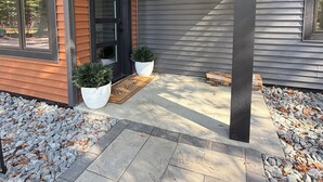 Een modern huis met een overdekte veranda, plantenpotten en een welkomstmat.