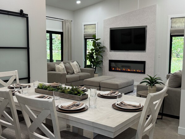 A modern living room with a fireplace, a flat-screen TV, and a dining area set for four. - Glimpse of Whitefish-Modern Home with SAUNA (Crosslake)