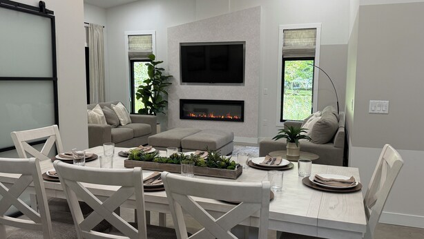 Een moderne woonkamer met een open haard, een flatscreen-televisie en een eethoek met witte meubels.