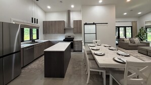 Een moderne keuken met een centraal eiland, inbouwmeubels en een eethoek met een lange tafel en stoelen.