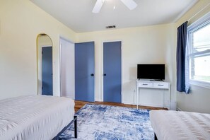 A bedroom with two beds, a TV, a desk, and a large window.