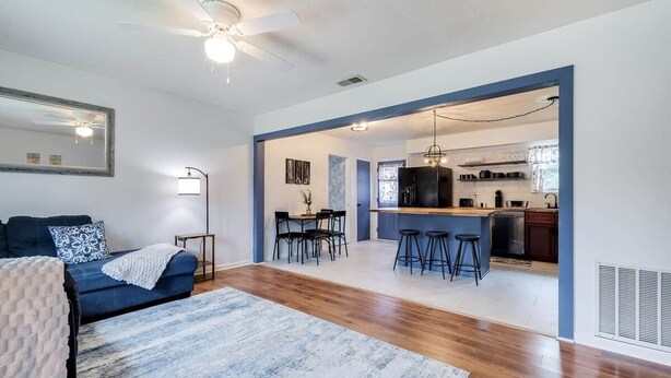 A modern living room with a blue sofa, a coffee table, and a large rug. There is a dining area with a table and chairs, and a kitchen in the background. - House of Smurf, Close to Savannah State (Savannah)