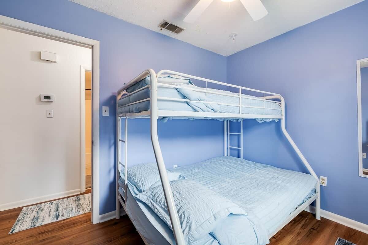 Habitación con literas de estructura metálica blanca, ropa de cama azul y suelo de madera.