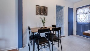 A dining area with a wooden table, black chairs, and a vase with plants. There are three framed pictures on the wall and a blue door with patterned curtains. - House of Smurf, Close to Savannah State (Savannah)