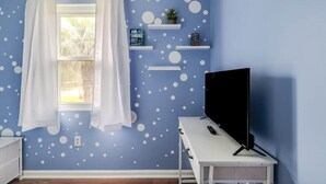 A room with a blue wall, white polka dot pattern, a window with white curtains, a TV on a white stand, and shelves with decorative items. - House of Smurf, Close to Savannah State (Savannah)