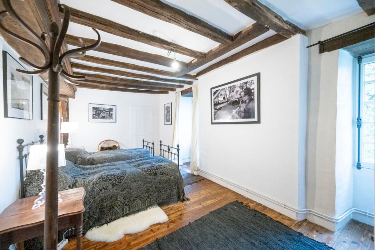 A bedroom with a bed, wooden beams, a chair, and a rug.