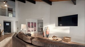 A modern living room with a leather sofa, a flat-screen TV mounted on the wall, and a dining area in the background. - Charming vacation rental steps away from River Island Golf Course (Porterville)
