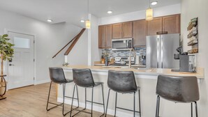 Une cuisine moderne avec des meubles en bois, des appareils en acier inoxydable et un coin bar avec des tabourets.