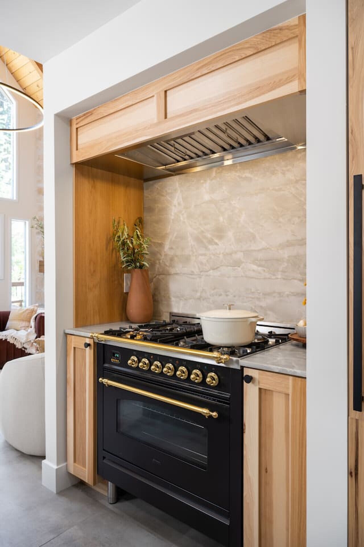 A modern kitchen with a black stove, wooden cabinets, and a marble backsplash.