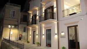 Un edificio de varios pisos con balcones, iluminación exterior y una escalera que conduce a la entrada.