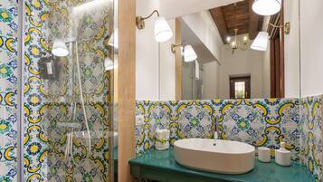 Un baño con salpicadero de azulejos estampados, un lavabo redondo y una ducha con puerta de cristal.