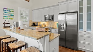 A modern kitchen with white cabinetry, a stainless steel refrigerator, a microwave, and a granite countertop.