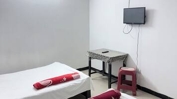 Une chambre avec deux lits, un ventilateur de plafond, un téléviseur fixé au mur, une petite table et un tabouret rouge.