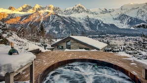 Eine Holzterrasse mit Whirlpool, einem Wintergarten und einem verschneiten Berg im Hintergrund.