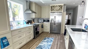 Una cucina moderna con mobili chiari, elettrodomestici in acciaio inossidabile, un'isola grande e un tappeto azzurro a motivi.