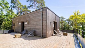 A wooden cabin with a deck, two lounge chairs, and a small table.