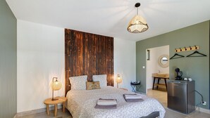 Una camera da letto con un letto, lampade da comodino, una parete d'accento in legno, una lampada a sospensione, un tavolino, uno specchio e un frigorifero.