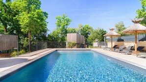Una piscina con lettini e ombrelloni, immersa nel verde alberato e delimitata da una recinzione.