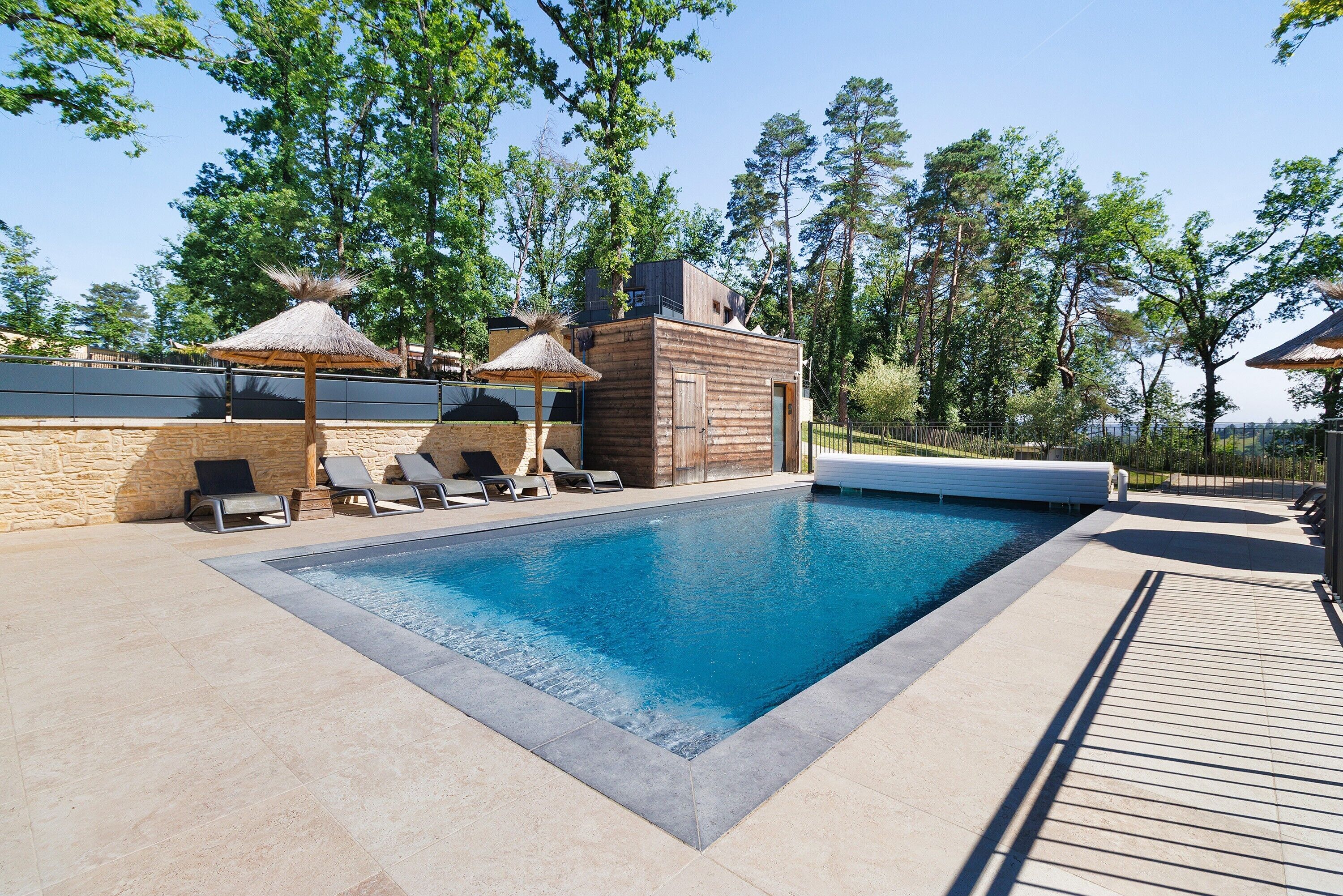 Une piscine avec des chaises longues et un bâtiment en bois doté d’un toit de chaume.