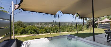A hot tub under a canopy with a view of a green landscape.