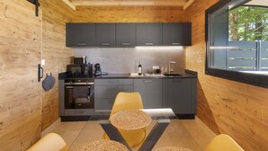 Une cuisine moderne aux murs en bois, un coin repas avec une chaise jaune et une fenêtre donnant sur des arbres.
