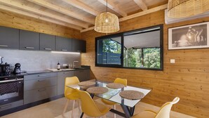 Une cuisine moderne avec des poutres en bois, une table à manger avec des chaises jaunes et une grande fenêtre donnant sur un paysage verdoyant.