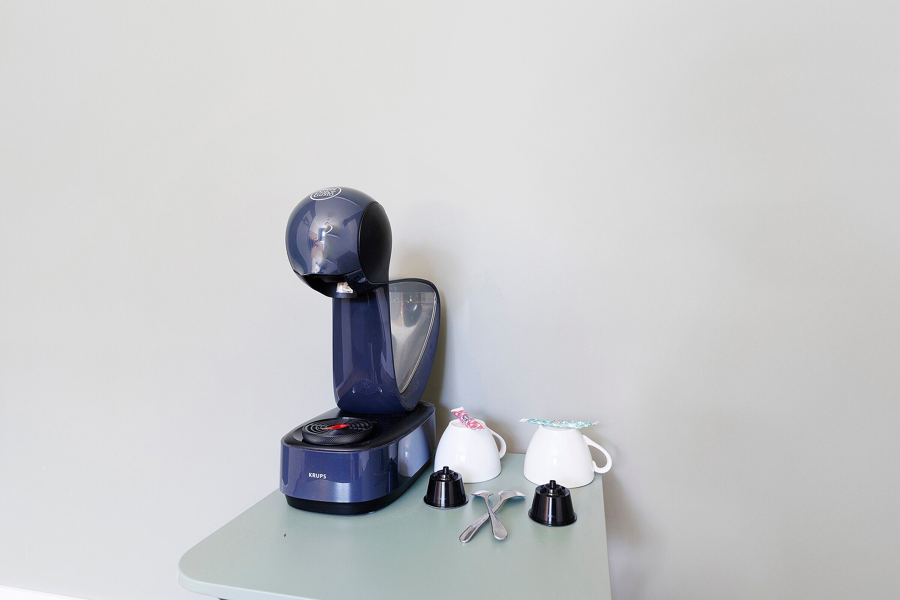 Una cafetera con una taza y una cuchara sobre una mesa.