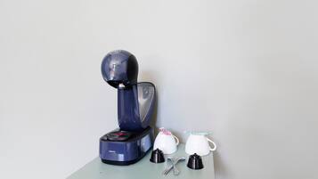 Una cafetera con una taza y una cuchara sobre una mesa.