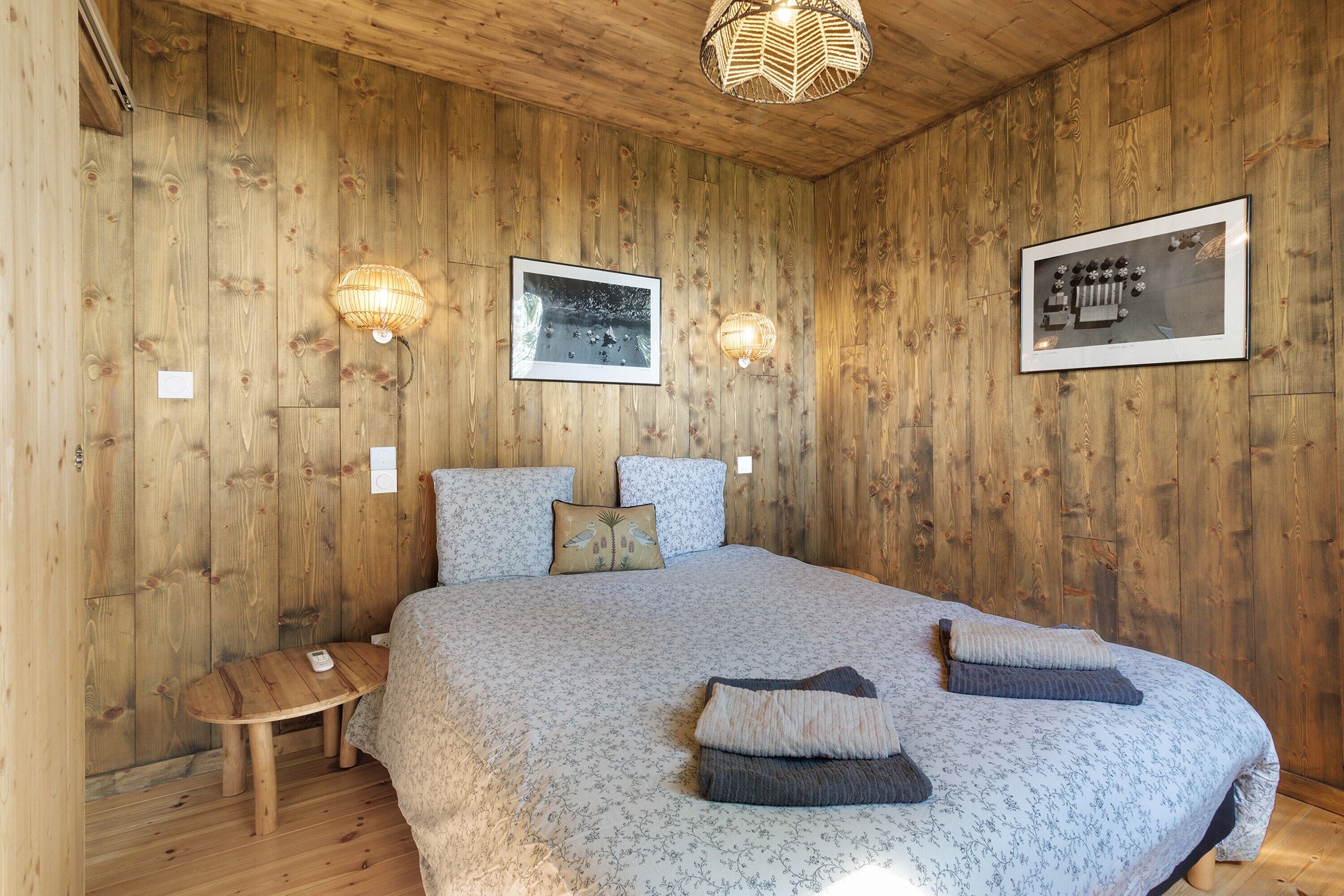 A wooden-paneled room with a bed, two wall-mounted lamps, and a framed picture.