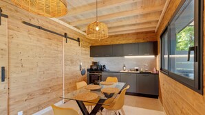 A modern kitchen with wooden walls, a glass dining table, and yellow chairs. - Le Pech Eternel - Lodge Spa Acacias (Sarlat la Canéda)