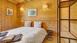 A wooden-paneled room with a bed, two wall-mounted lamps, and framed pictures.