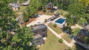 An aerial view of a modern residential area with multiple houses, a swimming pool, and a well-maintained lawn.