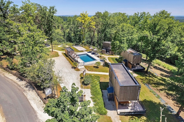 Un resort moderno con piscina, cabañas de madera y un césped cuidado.