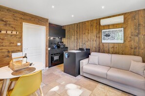 Un espacio habitable compacto con kitchenette, un sofá, una mesa de comedor con sillas y una pared decorativa de madera.